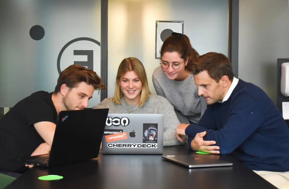 Four people collaborating around a laptop on a table in a modern office